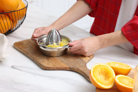 Making orange juice. Woman with juicer at white marble table indoors, closeupの写真素材