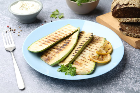 Delicious grilled courgette slices with parsley and lemon served on gray textured table, closeupの写真素材