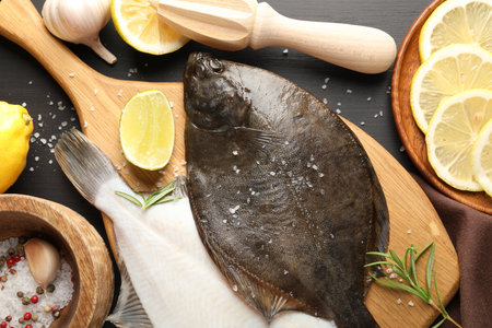 Fresh raw flounder fish, spices and juicer on black wooden table, flat lay. Seafoodの写真素材