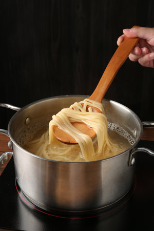 Woman taking boiled tagliatelle pasta with spoon from pot on electric stove, closeupの写真素材