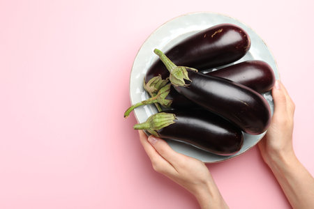 Woman with plate of fresh eggplants on pink background, top view. Space for textの写真素材