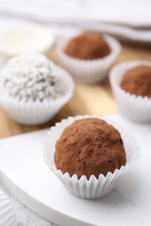 Homemade candies with cocoa powder and coconut flakes on table, closeup