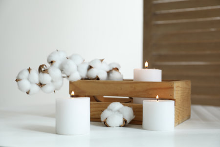 Crate with burning candles and cotton flowers on white table at homeの写真素材