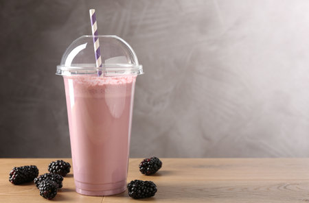 Tasty milkshake in plastic cup and blackberries on wooden table, space for textの写真素材