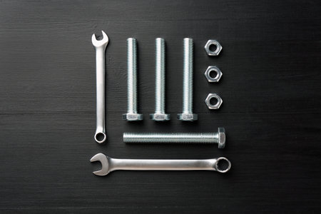 Many metal wrenches, bolts and nuts on black wooden table, flat lay