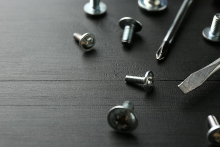 Many metal screwdrivers and bolts on black wooden table, closeupの写真素材