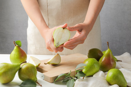 Woman cutting fresh ripe pear at white wooden table, closeupの写真素材