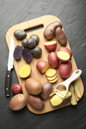 Different types of potatoes, peeler and knife on black table, flat layの写真素材