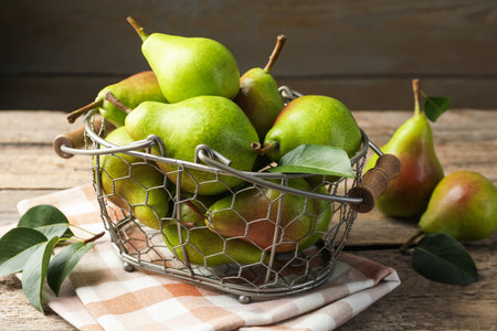 Fresh ripe pears in metal basket and green leaves on wooden table, closeupの写真素材