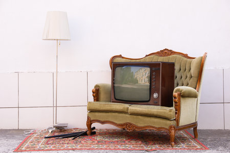 Retro TV on sofa, lamp and carpet near white wall outdoors.の写真素材