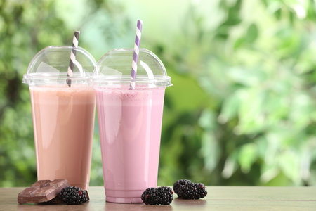 Tasty milkshakes in plastic cups and ingredients on wooden table outdoors, space for textの写真素材