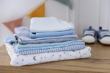 Stack of clean baby clothes and shoes on wooden table indoors, closeupの写真素材