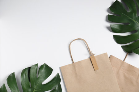 Eco friendly packaging. Paper bags and leaves on white background, flat lay. Space for textの写真素材