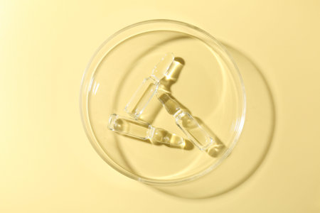 Glass ampoules with liquid and Petri dish on yellow background, top view