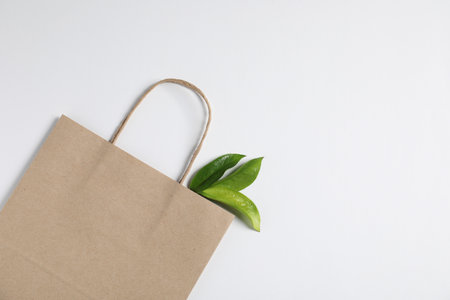 Eco friendly packaging. One paper bag and leaves on white background, top view. Space for textの写真素材