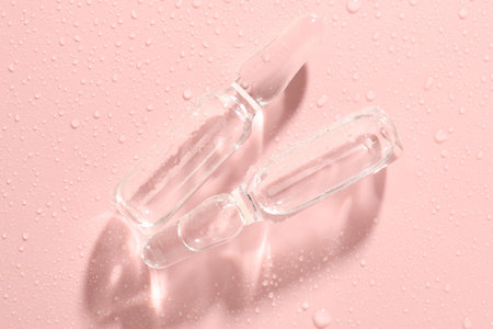 Glass ampoules with liquid and water drops on pink background, flat layの写真素材