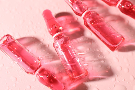Glass ampoules with liquid and water drops on pink background, above viewの写真素材