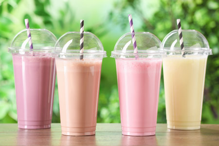 Tasty milkshakes in plastic cups on wooden table outdoorsの写真素材