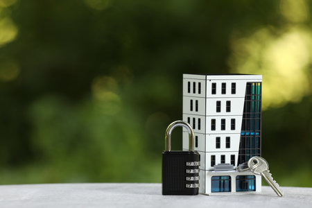 Home security. House model, key and padlock on light gray table outdoors, closeup. Space for textの写真素材