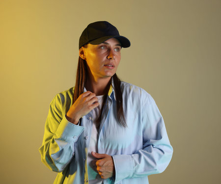 Beautiful woman wearing baseball cap in neon lights against color backgroundの写真素材