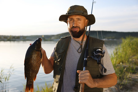 Fisherman holding rod and caught fish near lake at summer