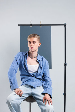 Handsome young man wearing stylish clothes sitting on chair against light grey background