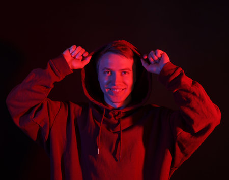 Portrait of smiling man wearing hoodie with crossed arms in neon lights against black backgroundの写真素材