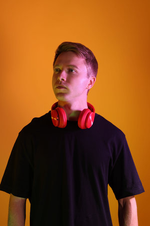 Handsome man with headphones in neon lights against orange background