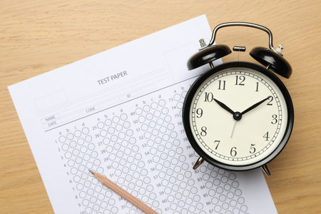 Answer sheet, pencil and alarm clock on wooden table, flat lay. Student passing examの写真素材