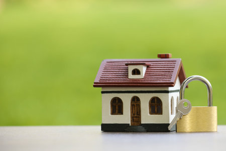 Home security. House model, key and padlock on white table outdoors, closeup. Space for textの写真素材