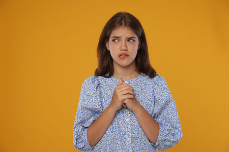 Student praying for good exam result on orange background