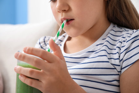Little girl drinking juice through straw on sofa at home, closeupの写真素材