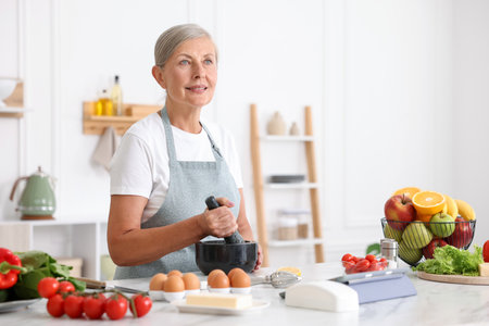 Senior woman cooking at white marble table in kitchenの写真素材