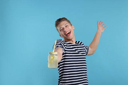 Happy man with mason jar of lemonade on light blue background. Refreshing drinkの写真素材