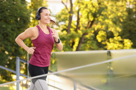 Athletic young woman with headphones in sportswear running outdoors, space for textの写真素材