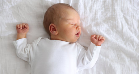 Cute newborn baby sleeping on bed, top view