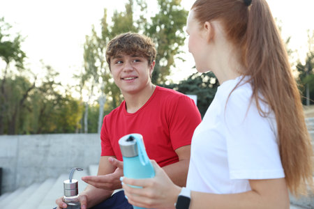 Teenage boy and girl with water bottles after training outdoors