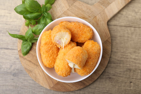 Delicious fried croquettes in bowl and basil on wooden table, flat layの写真素材