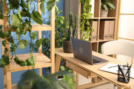 Stylish workplace with laptop, stationery and floral decor in office. Biophilic interior designの写真素材