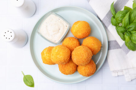 Delicious fried croquette balls, sauce and basil on light table, flat lay