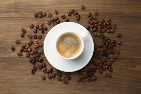 Aromatic coffee in cup and beans on wooden table, flat lay