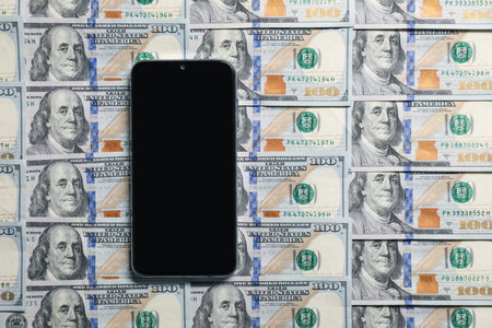 Smartphone on dollar banknotes as background, top view