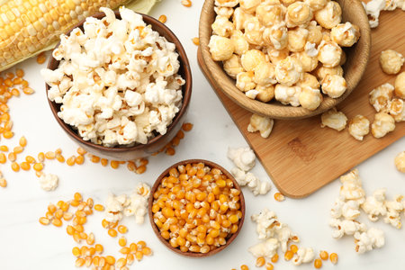 Tasty popcorn and corn kernels on white table, flat layの写真素材