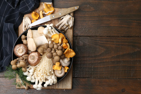Different raw mushrooms in bowl and knife on wooden table, top view. Space for textの写真素材