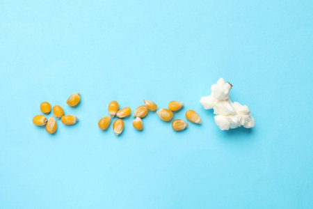 Tasty popcorn and dry kernels on light blue background, flat lay