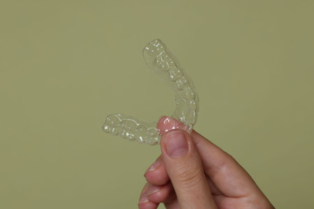 Woman with dental aligner on green background, closeup