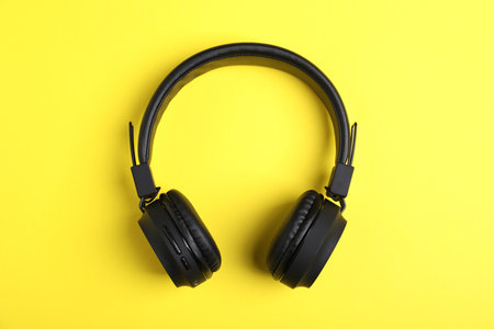 Pair of stylish black headphones on yellow background, top viewの写真素材