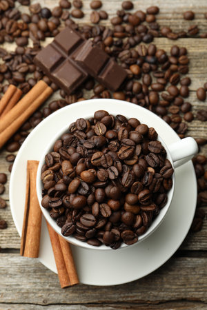 Aromatic coffee beans in cup, cinnamon and pieces of chocolate on wooden table, flat layの写真素材