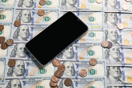 Smartphone and coins on dollar banknotes as background, closeupの写真素材