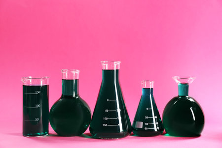 Laboratory glassware with green liquid on pink background. Space for textの写真素材